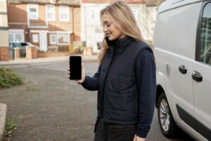 Tradesperson checking her phone for the next job while leaning against her van