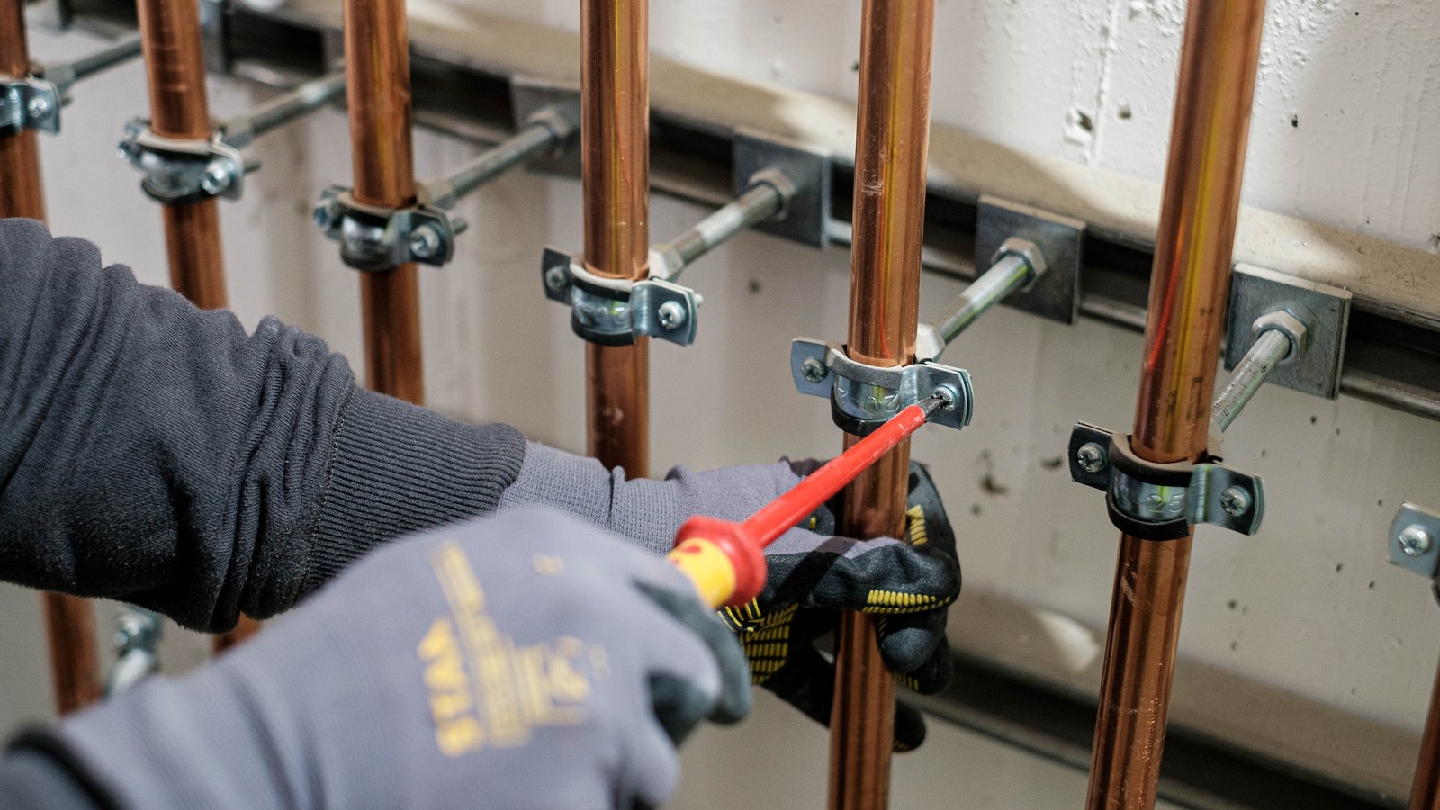 Tradesperson tightening pipework on a compliance-heavy installation